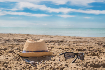 Sunglass and cap on sand against turquoise sea. T