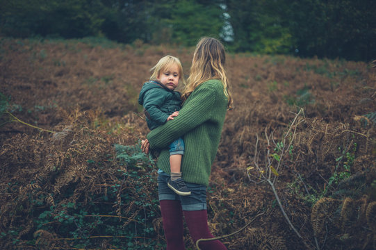 Young mother carrying toddler in meadow in autumn