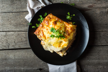 Piece of tasty hot lasagna with red wine. Small depth of field. Traditional italian lasagna. Portion. Italian food. Food on black plate. Bolognese sauce. Bechamel sauce. Still life of food. - obrazy, fototapety, plakaty