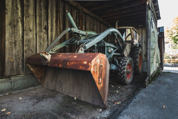 Naklejka premium Alte Eicher Zugmaschine mit Hubarm und Schaufel in einem dunklen Holzschuppen, Bayern, Deutschland