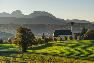 Die barocke Wallfahrtskirche in Wilparting und bunte Herbstwälder vor dem Wendelstein in der Morgensonne, Bayern, Deutschland © Matthias Riedinger
