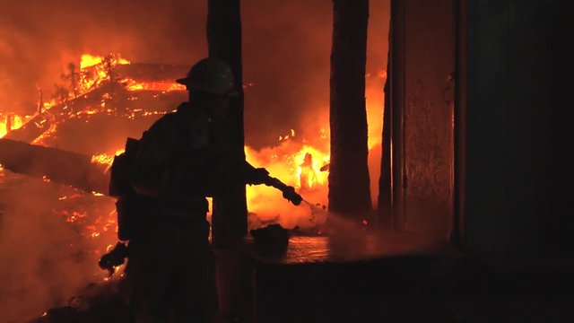 Firefighter hosing down outbuiliding at night and building fireline