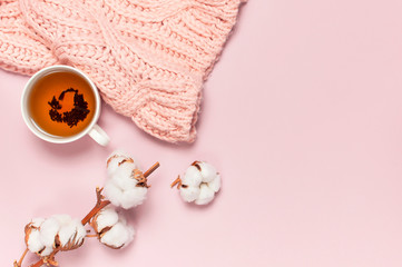 Female pink knitted sweater, branch of cotton, cup of tea on pastel pink background top view flat lay. Lady winter Clothes fashion look. Delicate cotton flowers. Lifestyle gentle female background