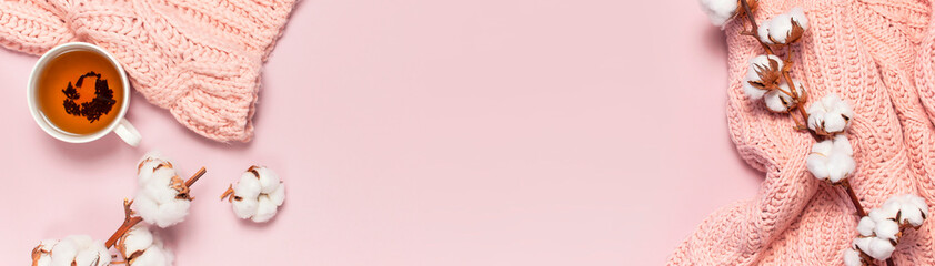 Female pink knitted sweater, branch of cotton, cup of tea on pastel pink background top view flat...