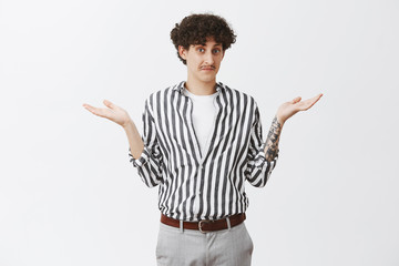 Waist-up shot of clueless good-looking and funny unaware guy with moustache and curly dark hair shrugging with spread palms having no idea feeling uncertain how to act or what answer