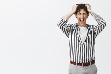 Studio shot of depressed young guy with moustache in striped shirt losing temper screaming out loud...
