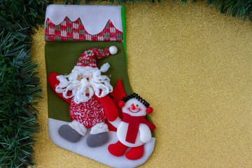 Green Christmas Stocking with Santa and Snowman. Green Tinsel. Golden Background. Copy Space. Top View