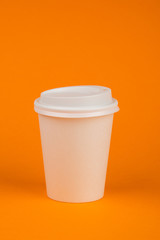 Paper container for coffee with a white cap on an orange background. Take-away beverage container. Drink Cup template for your design
