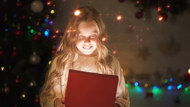 Adorable blond girl opening gift box, magic Christmas atmosphere, glowing effect