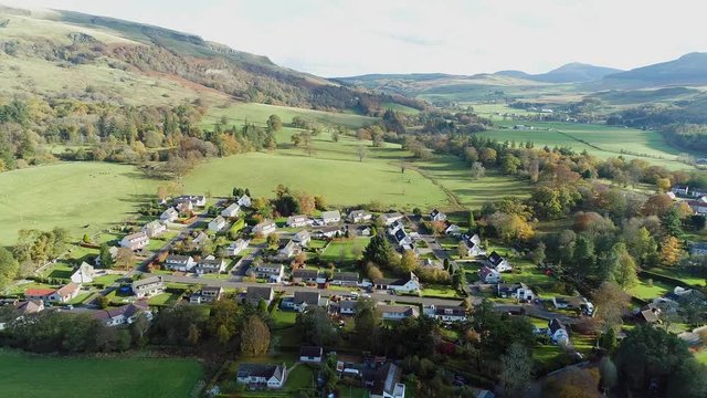 Aerial footage over the rural village of Fintry with views to the Campsie Fells. Flying away.