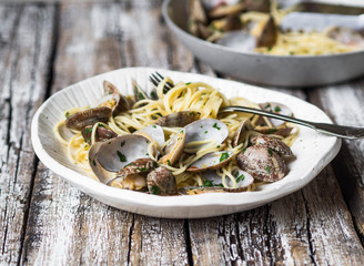 Spaghetti with clams, garlic and parsley in a white bowl and pan with pasta on an old wooden background