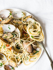 Spaghetti with clams, tomatoes, garlic and parsley on a white plate and rustic fork on a white background. Top view