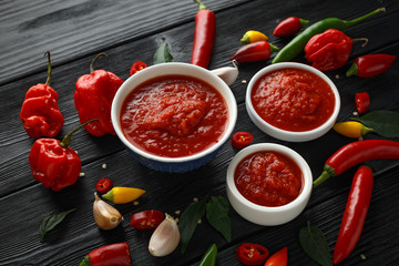 spicy hot sweet chili sauce with mix of chilli pepper, garlic and tomatoes on rustic wooden...