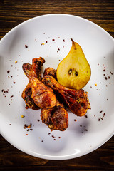 Grilled chicken drumsticks with pear on wooden background