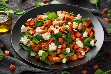 Healthy roasted sweet potato salad with spinach, feta cheese, hazelnut nuts in black plate, rustic...
