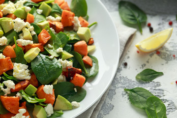 Avocado, roasted sweet potato, spinach, feta cheese healthy salad in white plate.