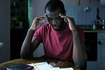 Unpaid debt problems. Young unhappy african american man trying to figure out details of bills,...