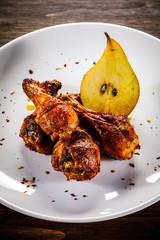 Grilled chicken drumsticks with pear on wooden background