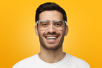 Optimistic young man smiling, showing white perfect teeth, isolated on yellow background. Positive emotions and happiness concept