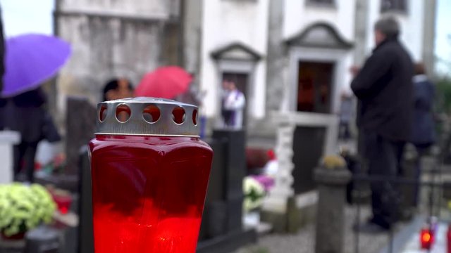 A candle on a cemetery with a priest preaching and a man crosses himself. 