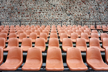Fototapeta premium Rows of brown plastic chairs on the background of the old stone wall.