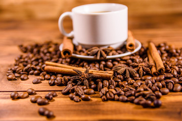 Cup of hot coffee, star anise, cinnamon sticks and scattered coffee beans on wooden table