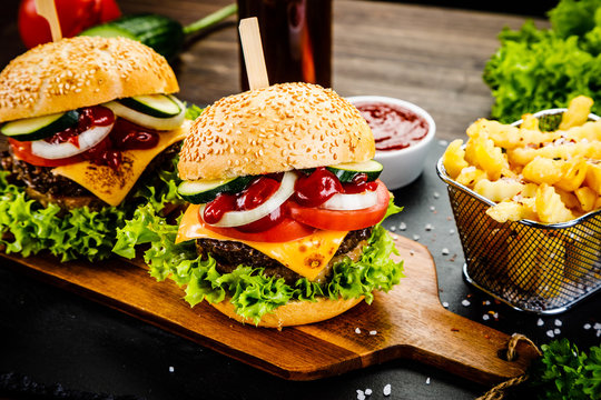 Tasty burgers with chips served on cutting board on stone plate