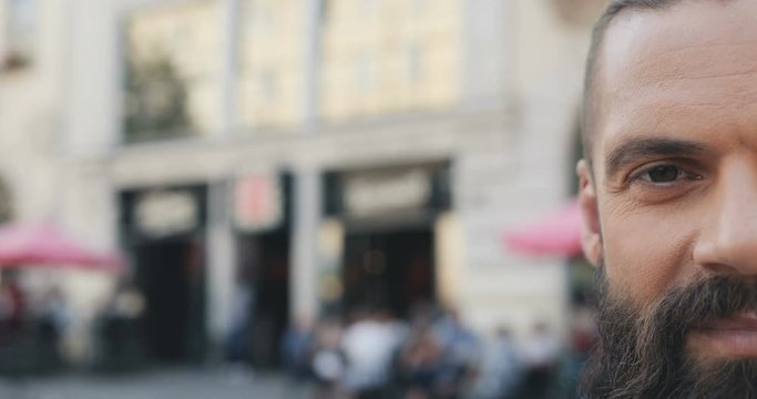 Close up of the serious half face of the good looking hipster man withe a beard looking straight to the camera and smiling. Portrait. Outside.