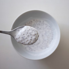 Spoon above the white plate of chia seeds with coconut milk, top view