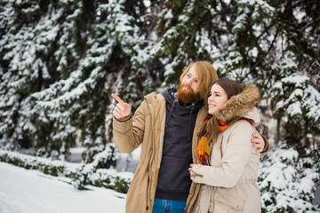 Obraz premium Young Caucasian boy and girl in love heterosexual couple have a date outdoors in a winter park on the background of a snowy conifer standing in an embrace. Man hugging woman valentines day