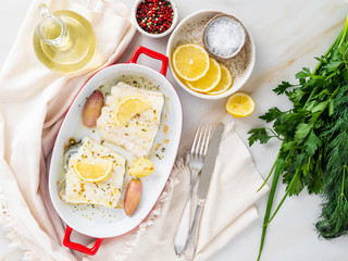 cod fish fillet, freshly cooked in oven with onion in porcelain dish for baking, lemon on plate, top view