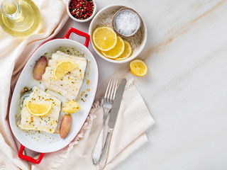 cod fish fillet, freshly cooked in oven with onion in red porcelain dish for baking, lemon, top view, copy space