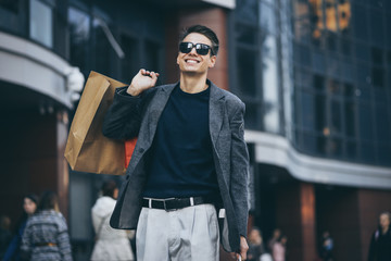 Serious stylish young man with sunglasses walking in urban street and enjoying Black Friday shopping in trendy stores in city