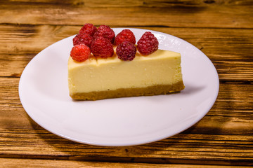 White plate with cheesecake New York and raspberries on wooden table