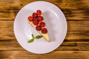 White plate with cheesecake New York, leaf of mint and raspberries on wooden table. Top view