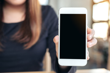 Mockup image of a woman holding and showing white mobile phone with blank screen on the table in modern cafe