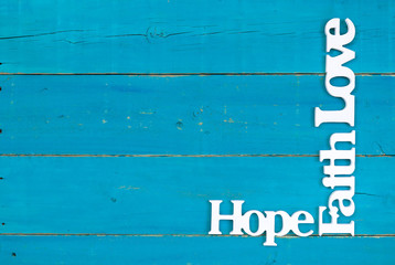 Hope, Faith and Love hanging on rustic teal blue wood background; spiritual background with copy space