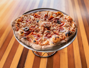 Gourmet Italian Meat Pizza on pizza stand and wooden table