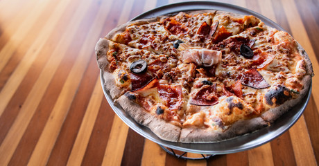 Gourmet Italian Meat Pizza on pizza stand and wooden table