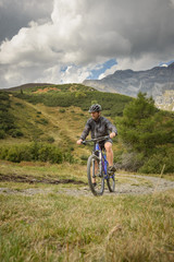 Mountain biker on the mountain pasture with mountains and blue sky as a background, traveling alone, on the corona time, 