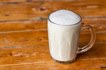 Glass of warm fresh milk with froth on wooden table top