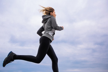 Teen girl in sportswear runs against cloudy sky