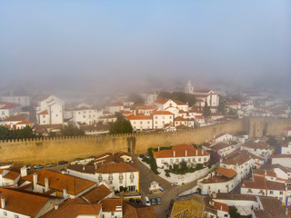 Scenic view of white houses red tiled roofs, and castle from wall of fortress with clouds. Obidos village, Portugal.