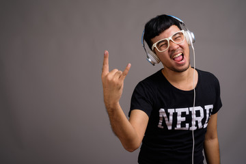 Young Asian nerd man listening to music against gray background