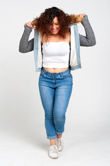 Body positive concept. Smiling curly girl plus size, dressed in casual style, posing at ease in the studio for white background. Emotions.
