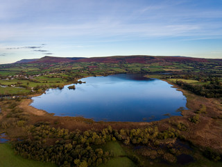 Aerial panoramic view of a beautiful natural lake in Brecon Beacons surrounded by rural farmland (Llangorse Lake, Wales)