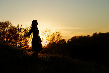 silhouette of a young woman descending from a hill at sunset, a girl walking in the autumn in the field