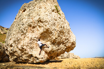 Man climbing a giant rock boulder on rocky terrain in Malta