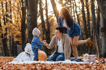 happy family with little cute child in park on yellow leaf with big pumpkin in autumn