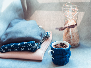 Fototapeta na wymiar Cup of coffee beans, warm woolen sweaters, decorated with led lights, side view point. Autumn weekend concept. Cozy home. Still life details of living room. Toned. Selected focus